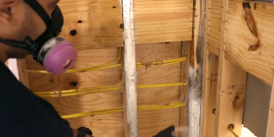Technician wearing a respirator inspecting exposed wall framing and studs for mold growth